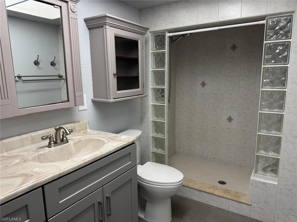 Image 2: Full bathroom with vanity, dual sink a textured wall, a shower stall, and light tile patterned floors
