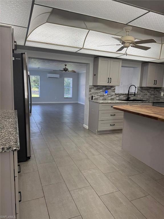 Image 4: Kitchen with ceiling fan, open floor plan, gray cabinetry, decorative backsplash, and light stone counters