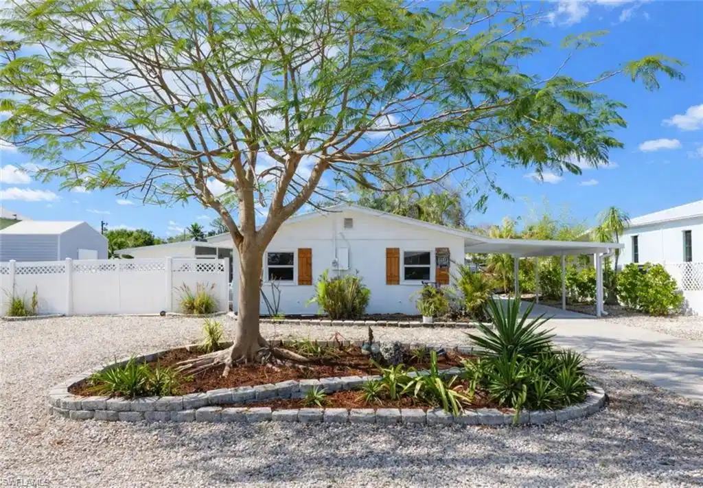 Image 1: White single-story residence with a carport and gravel driveway
