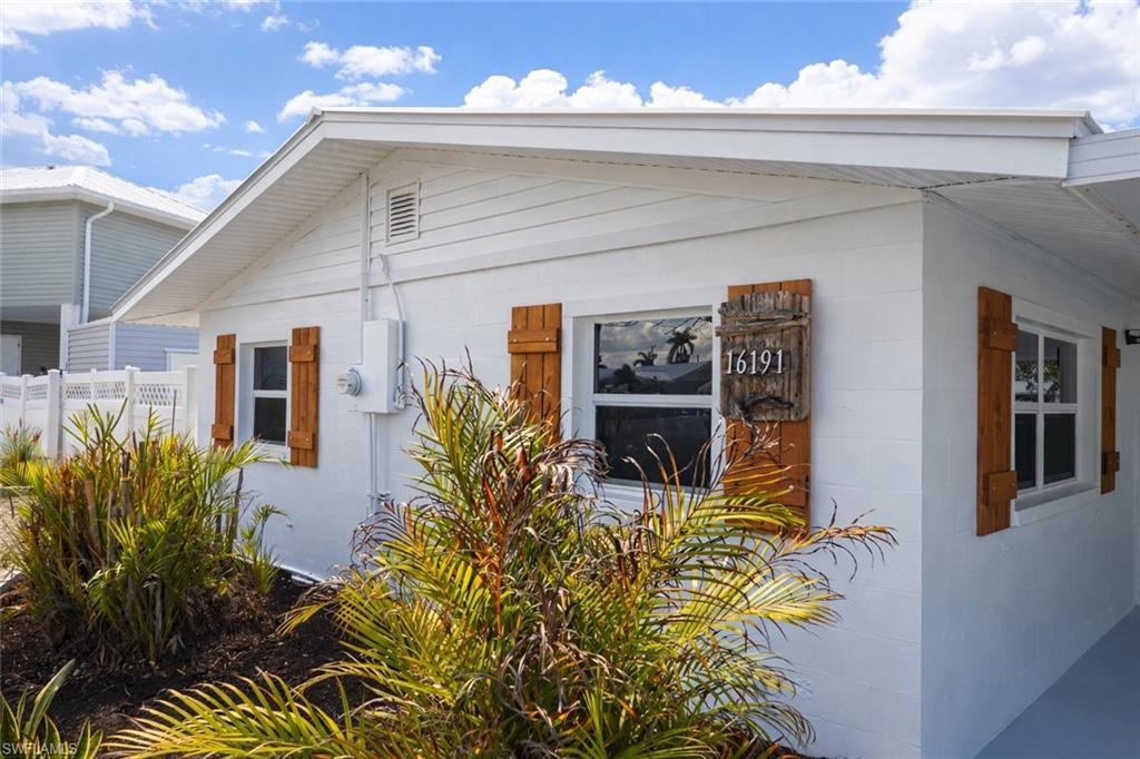 Image 2: Exterior featuring white siding and block construction, wood-finish shutters, white-framed windows, a decorative address plaque, and manicured landscaping
