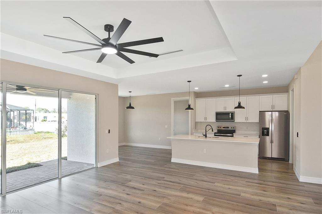 Image 4: Open-concept living space featuring wood-finish flooring, a tray ceiling with a modern ceiling fan, and sliding glass doors providing access to the outdoor patio