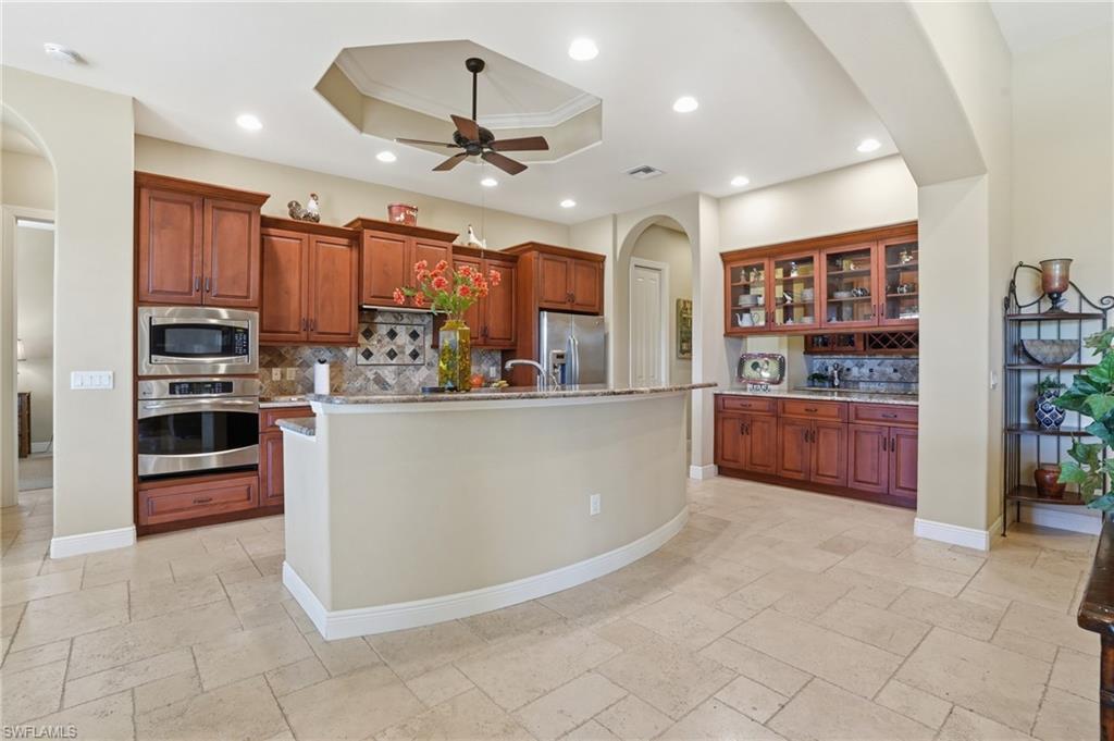 Image 4: Kitchen featuring arched walkways, stainless steel appliances, a tray ceiling, glass fronted cabinets, and crown molding