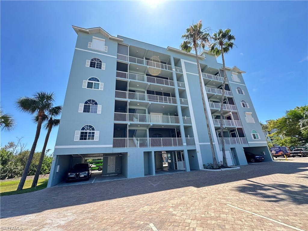 Image 3: Multi-story residential building featuring a light blue exterior, multiple balconies, arched windows with white shutters, and ground-level covered parking