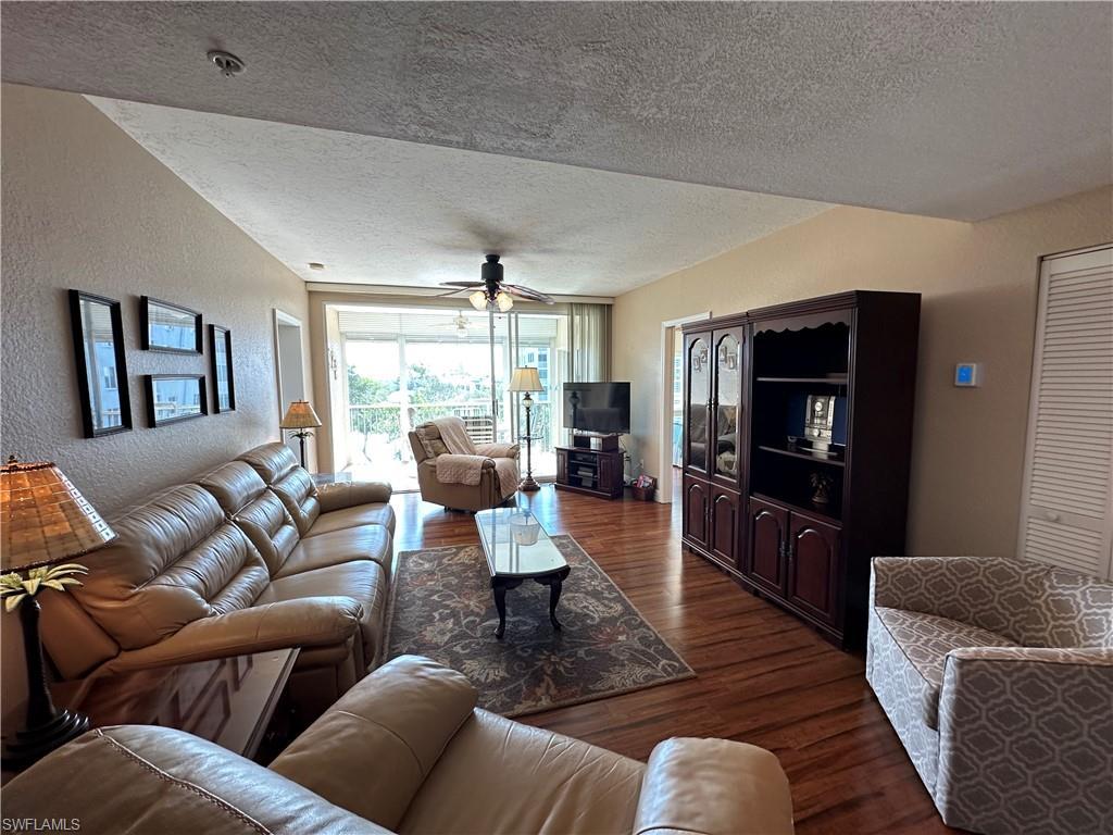 Image 4: Spacious living area featuring wood-finish flooring, a ceiling fan, and access to an outdoor patio with white railings