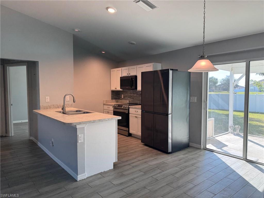 Image 2: Kitchen featuring appliances with stainless steel finishes, light countertops, decorative backsplash, white cabinets, and a peninsula