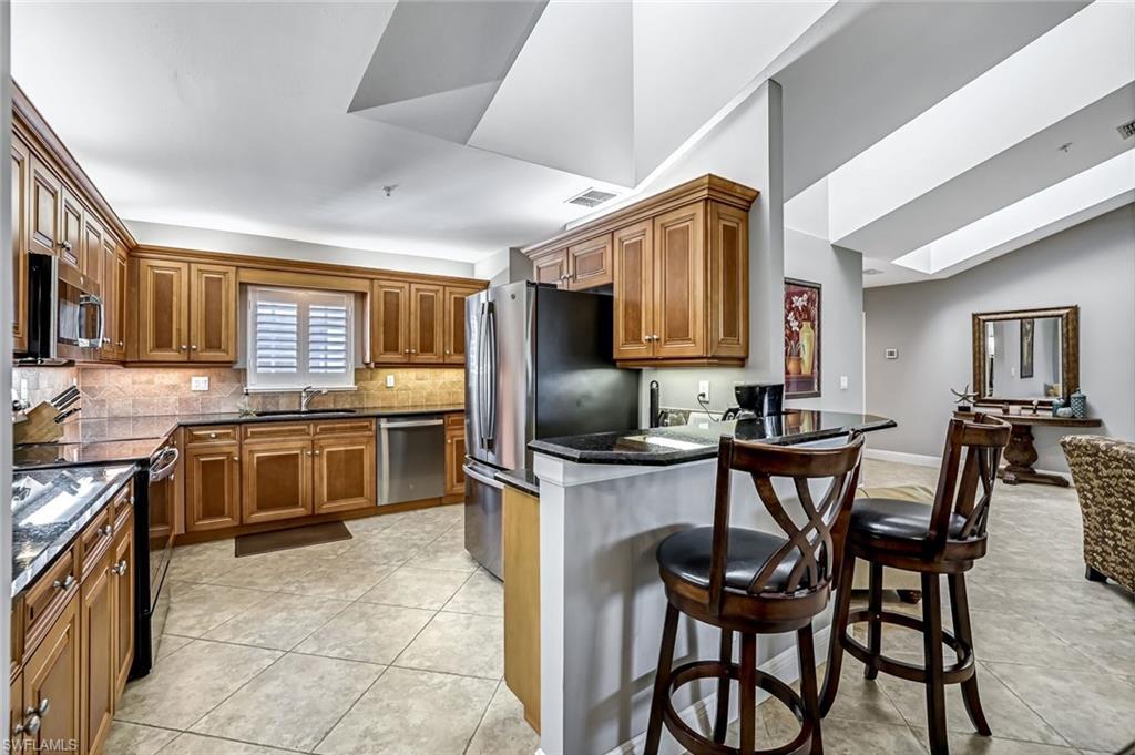 Image 3: Kitchen with wood finish cabinetry, a kitchen bar, stainless steel appliances, light tile floors, and lofted ceiling
