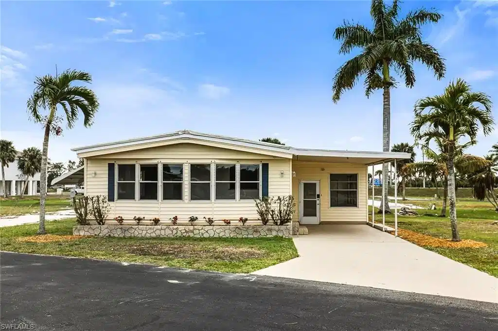 Image 1: Single-story residence featuring light-colored siding, a covered carport, and multiple windows with dark shutters