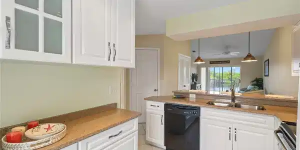 Image 3: Kitchen with white cabinets, glass insert cabinets, black dishwasher, light stone counters, and light tile patterned floors