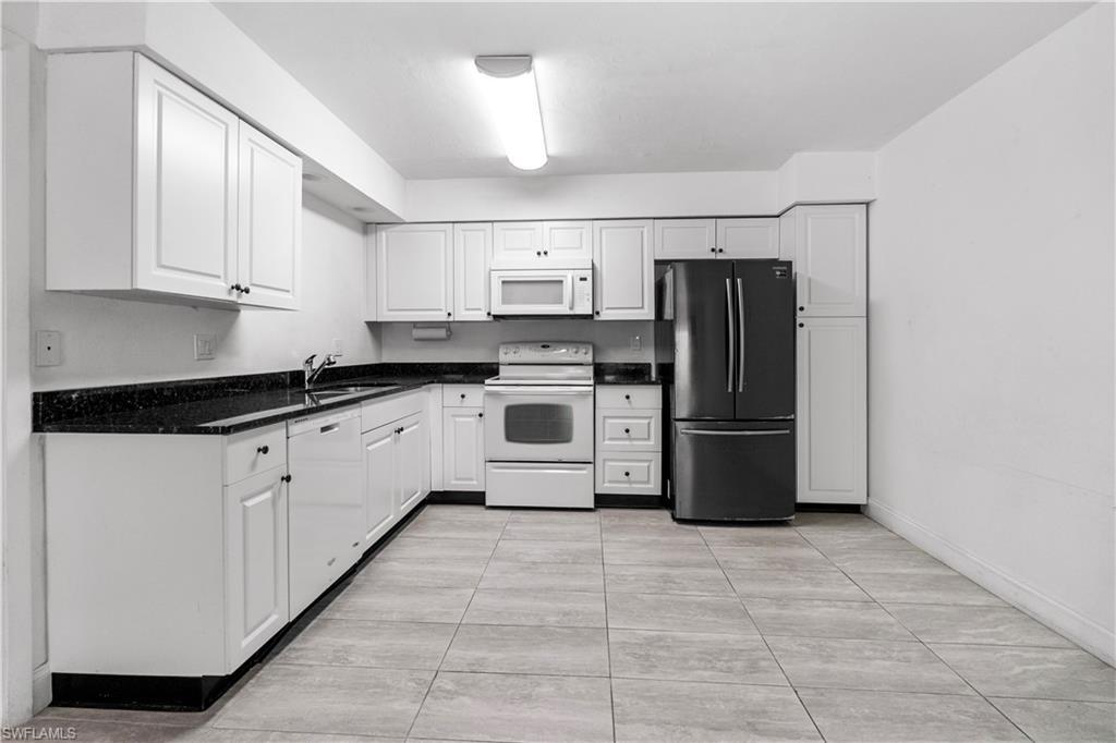 Image 1: Kitchen with white appliances, white cabinets, dark stone counters, and light tile patterned floors