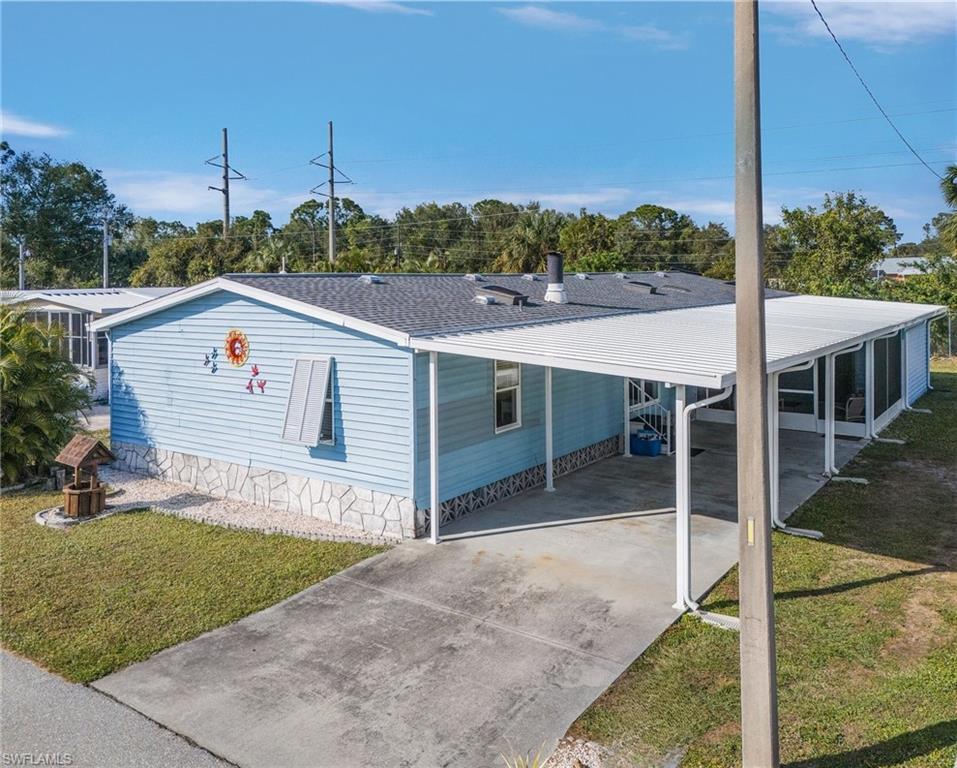Image 2: Overview of the property featuring a front yard, concrete driveway, an attached carport, and roof with shingles