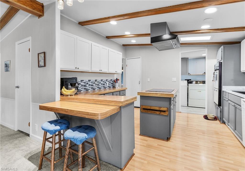 Image 3: Kitchen with a breakfast bar, wood counters, a peninsula, tasteful backsplash, and extractor fan
