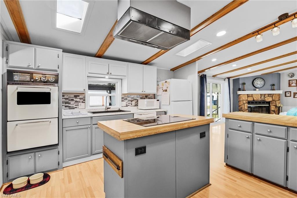 Image 4: Kitchen featuring a center island, wall chimney exhaust hood, gray cabinetry, beam ceiling, and white appliances