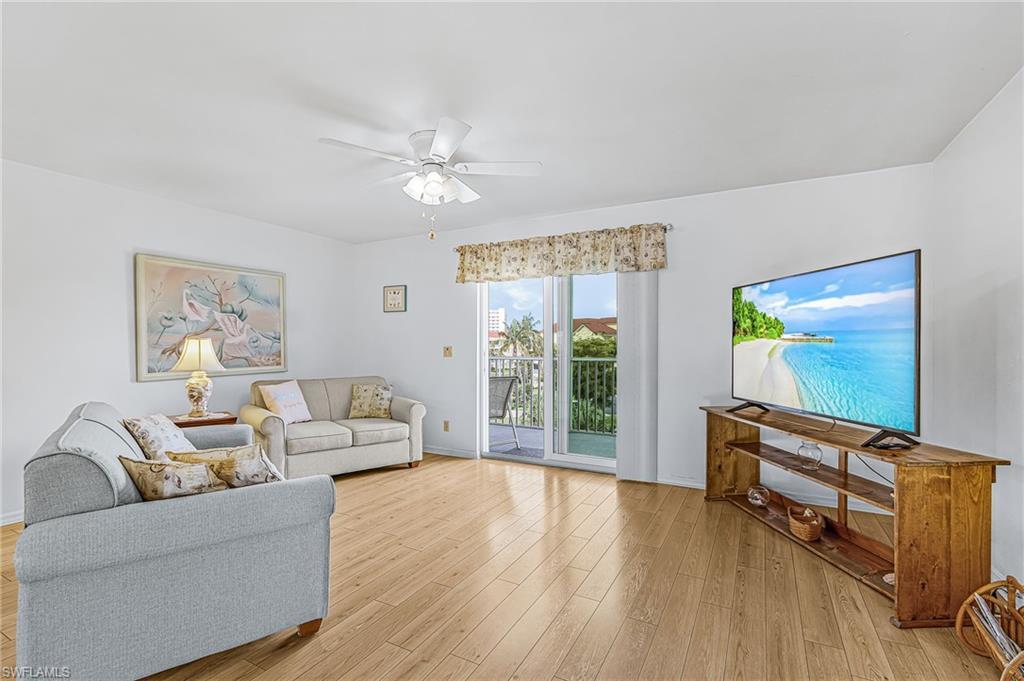 Image 3: Bright living area featuring wood-finish flooring, a ceiling fan with integrated lighting, and a sliding glass door leading to an outdoor balcony