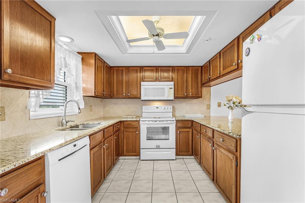 Image 4: U-shaped kitchen featuring wood cabinetry, granite countertops, white appliances, and a skylight with a ceiling fan