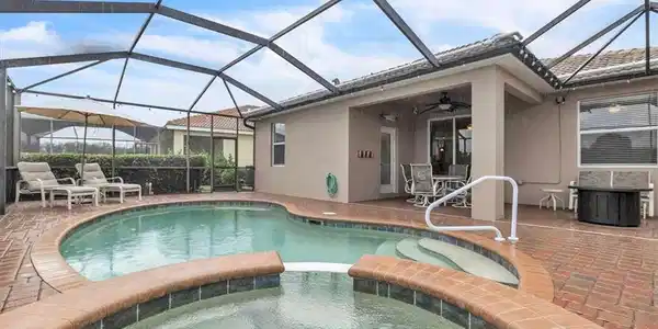 Image 2: Screened outdoor living area featuring a pool, integrated spa, brick paver decking, and a covered patio