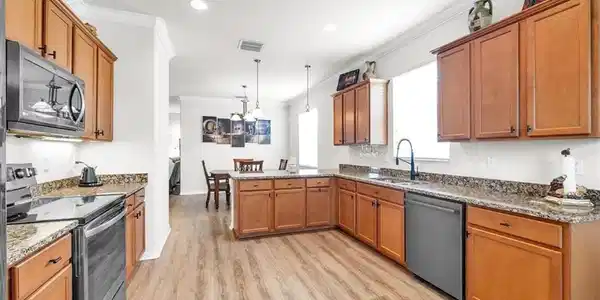 Image 4: L-shaped kitchen with wood-finish flooring, light wood cabinetry, stone countertops, and stainless steel appliances