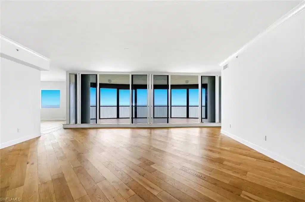 Image 1: Expansive living area featuring wood-finish flooring, a full wall of floor-to-ceiling windows, and a private balcony with metal railings