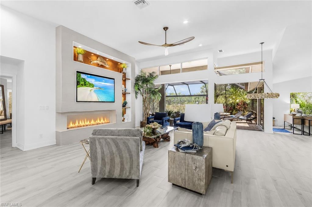 Image 3: Spacious living area featuring light wood-finish tile flooring, a contemporary fireplace and vaulted ceilings