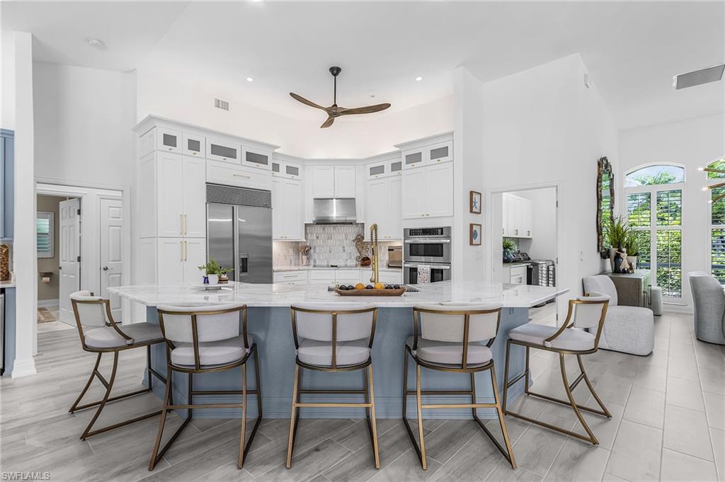 Image 4: Expansive kitchen featuring a large central island with seating for five, white cabinetry with upper glass-front accents, stainless steel appliances, and a tiled backsplash