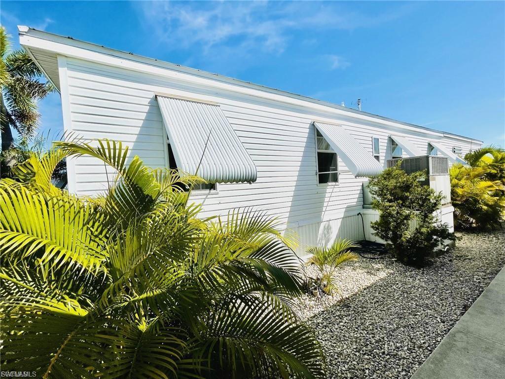 Image 4: White horizontal siding exterior with multiple window awnings, featuring a gravel perimeter and tropical landscaping