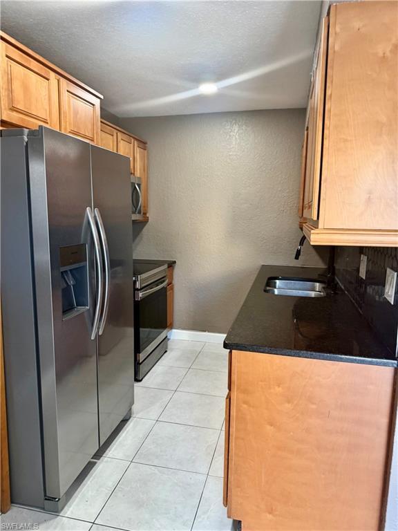 Image 4: Kitchen featuring stainless steel appliances, light wood cabinetry, dark countertops, and tile flooring