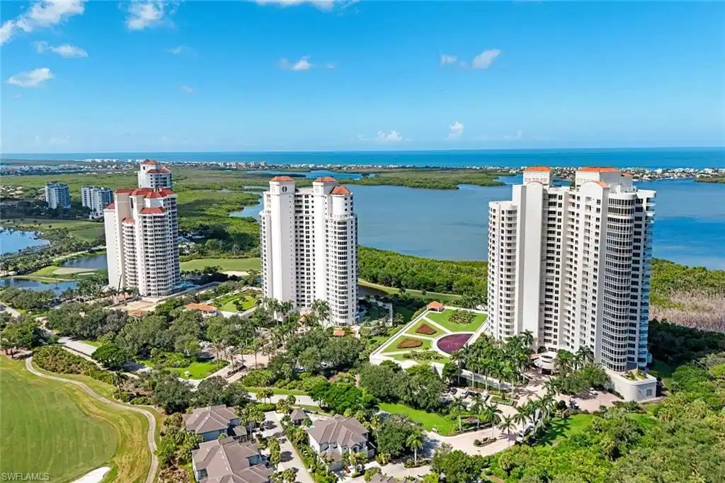 Image 1: Waterfront high-rise residences featuring modern tower architecture with floor-to-ceiling windows, manicured landscaping with mature trees and expansive green spaces, direct water access, and panoramic vistas of the coastal waterway and surrounding preserve lands