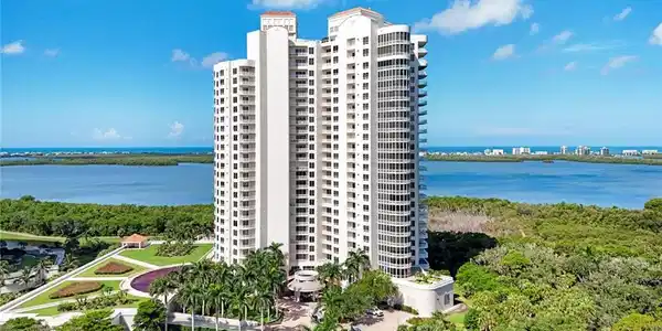 Image 2: Waterfront high-rise residential tower featuring contemporary white exterior, multiple stories with extensive fenestration, manicured landscaping with mature palm trees, and direct water and natural preserve vistas from an elevated position
