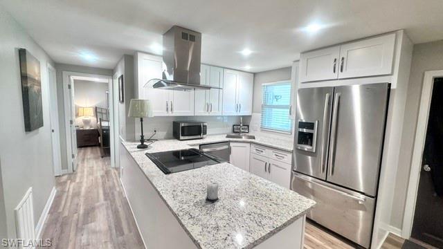 Image 2: Modern kitchen featuring a central island with a built-in cooktop, white shaker cabinetry, stainless steel appliances, and granite countertops