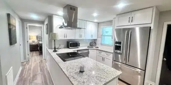 Image 2: Modern kitchen featuring a central island with a built-in cooktop, white shaker cabinetry, stainless steel appliances, and granite countertops