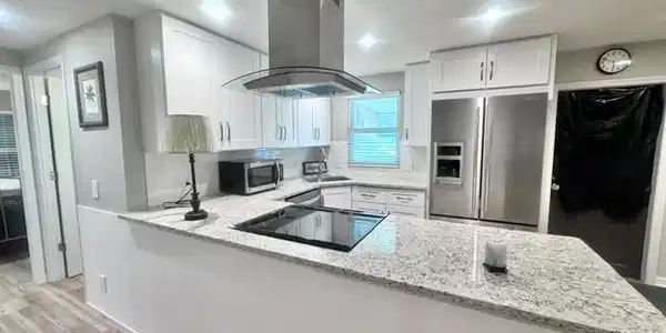 Image 3: Modern kitchen featuring white shaker cabinetry, stainless steel appliances, a built-in cooktop, and speckled light-tone countertops