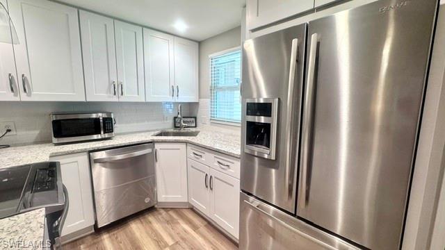 Image 4: Kitchen featuring white shaker cabinetry, stainless steel appliances, speckled countertops, a white subway tile backsplash, and wood-finish flooring