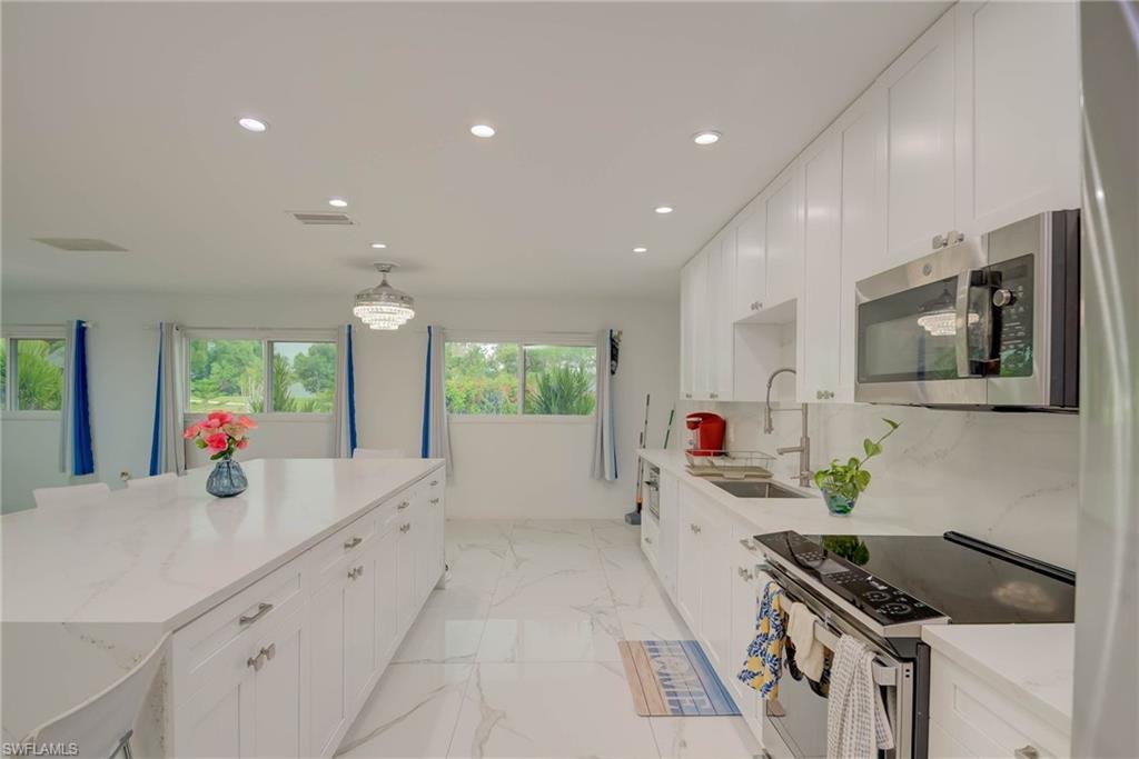 Image 4: Spacious kitchen featuring white cabinetry, stainless steel appliances, a large center island, recessed lighting, and expansive windows