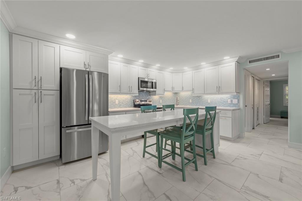 Image 4: Kitchen featuring appliances with stainless steel finishes, crown molding, white cabinets, light marble finish flooring, and backsplash