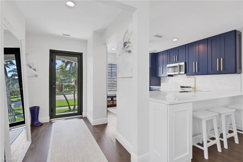 Image 3: Kitchen featuring blue cabinets, backsplash, a kitchen breakfast bar, light stone countertops, and stainless steel microwave