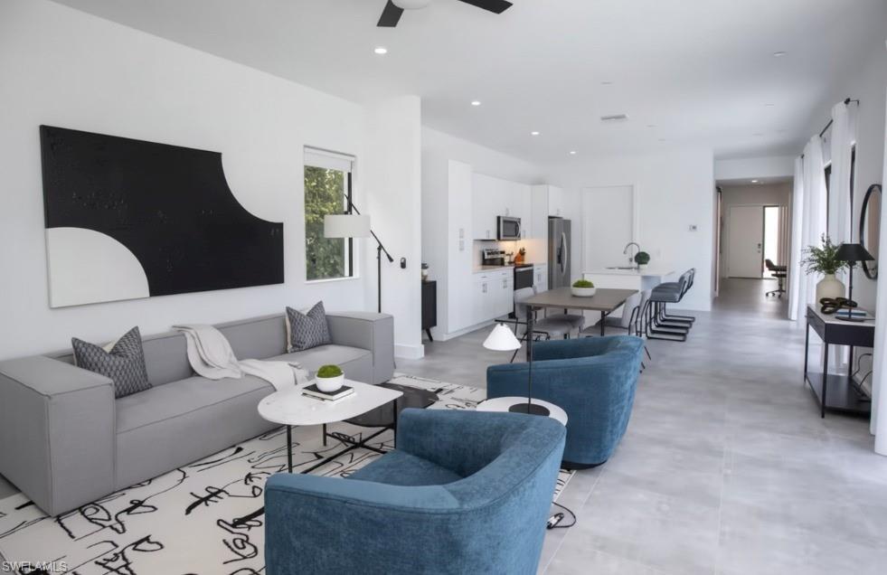Image 3: Open-concept living space featuring light gray tile flooring, a contemporary ceiling fan, recessed lighting, and a kitchen with white cabinetry and stainless steel appliances