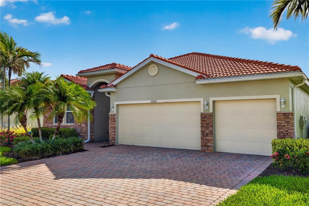 Image 2: Stucco exterior residence featuring a red tile roof, paver driveway, two-car garage, and stone accents