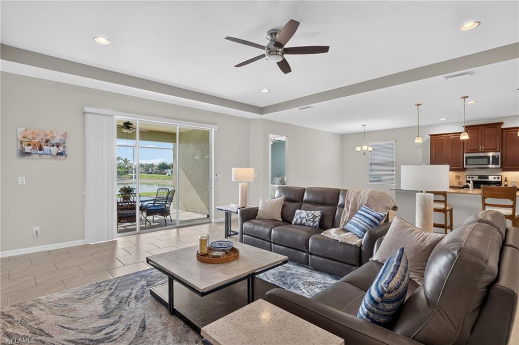 Image 3: Spacious open-concept living area featuring large format tile flooring, a tray ceiling with recessed lighting and a ceiling fan, and sliding glass doors opening to a screened lanai
