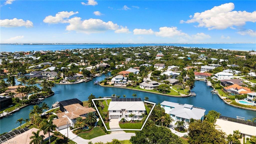 Image 3: Waterfront property featuring a white multi-story exterior, an attached garage, a paved driveway, mature landscaping, and solar panels