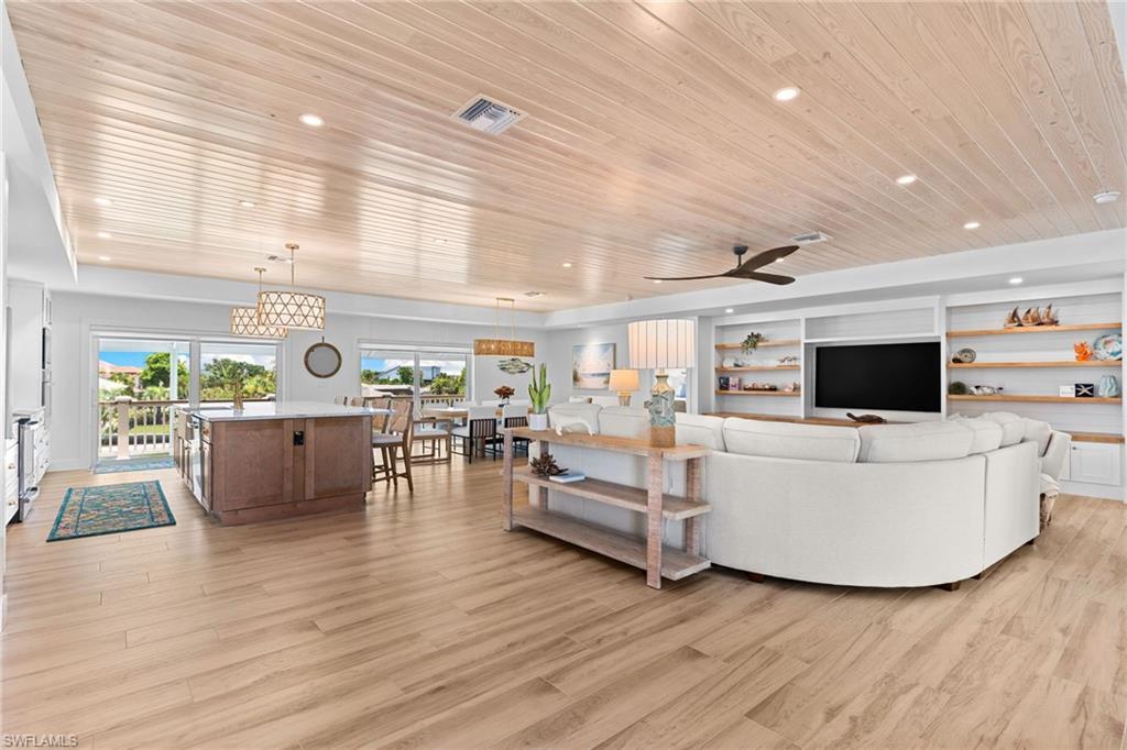 Image 4: Spacious open-concept living area featuring wood-finish flooring, a shiplap ceiling with recessed lighting, and a built-in media center with shelving