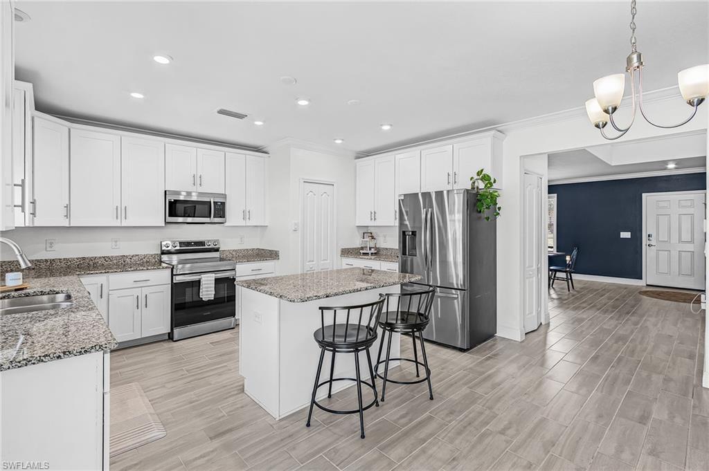 Image 2: Kitchen featuring white cabinetry, granite countertops, stainless steel appliances, a center island with seating, and wood-look tile flooring