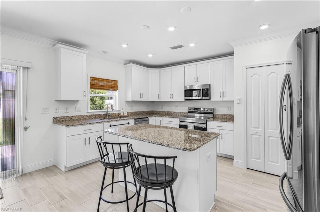 Image 3: Contemporary kitchen featuring an island with a granite countertop, white shaker cabinetry, stainless steel appliances, and wood-finish tile flooring