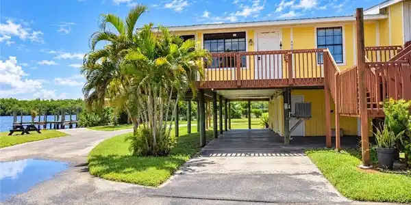 Image 2: Elevated coastal residence with a yellow exterior, expansive wooden deck with railing, and a covered parking area