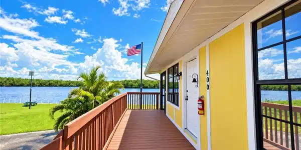 Image 4: Waterfront property featuring a wood-finish deck, yellow exterior siding with white trim, and dark-framed windows