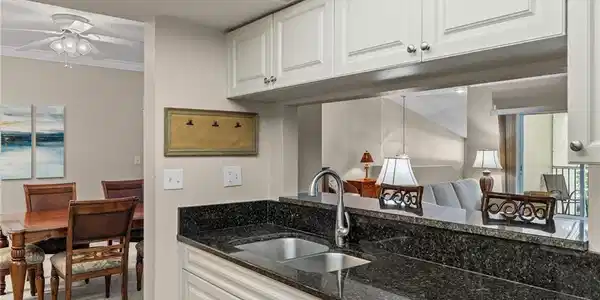 Image 4: Kitchen with white cabinetry, crown molding, ceiling fan, dark stone counters, and sink