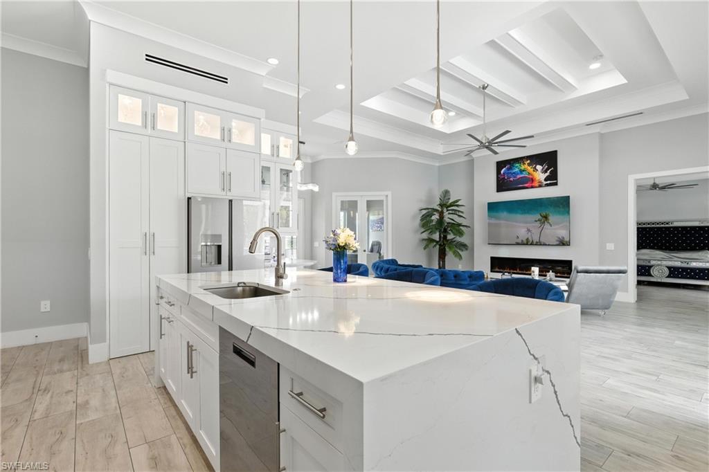 Image 1: Kitchen with dishwasher, a ceiling fan, ornamental molding, a center island with sink, and light stone counters