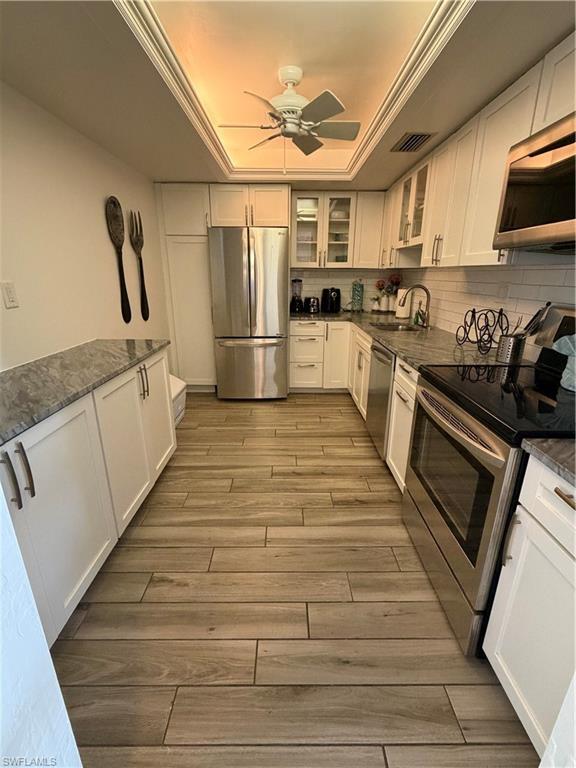Image 3: Kitchen featuring stainless steel appliances, white cabinets, glass insert cabinets, a raised ceiling, and ceiling fan