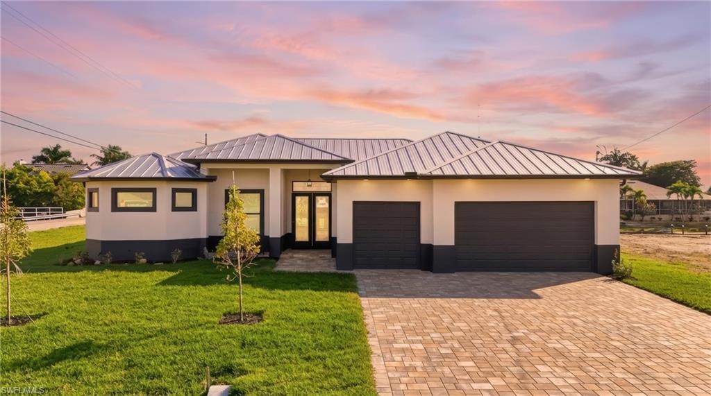 Image 1: New construction home featuring an attached garage, a standing seam roof, a landscaped front yard, decorative driveway, and stucco siding