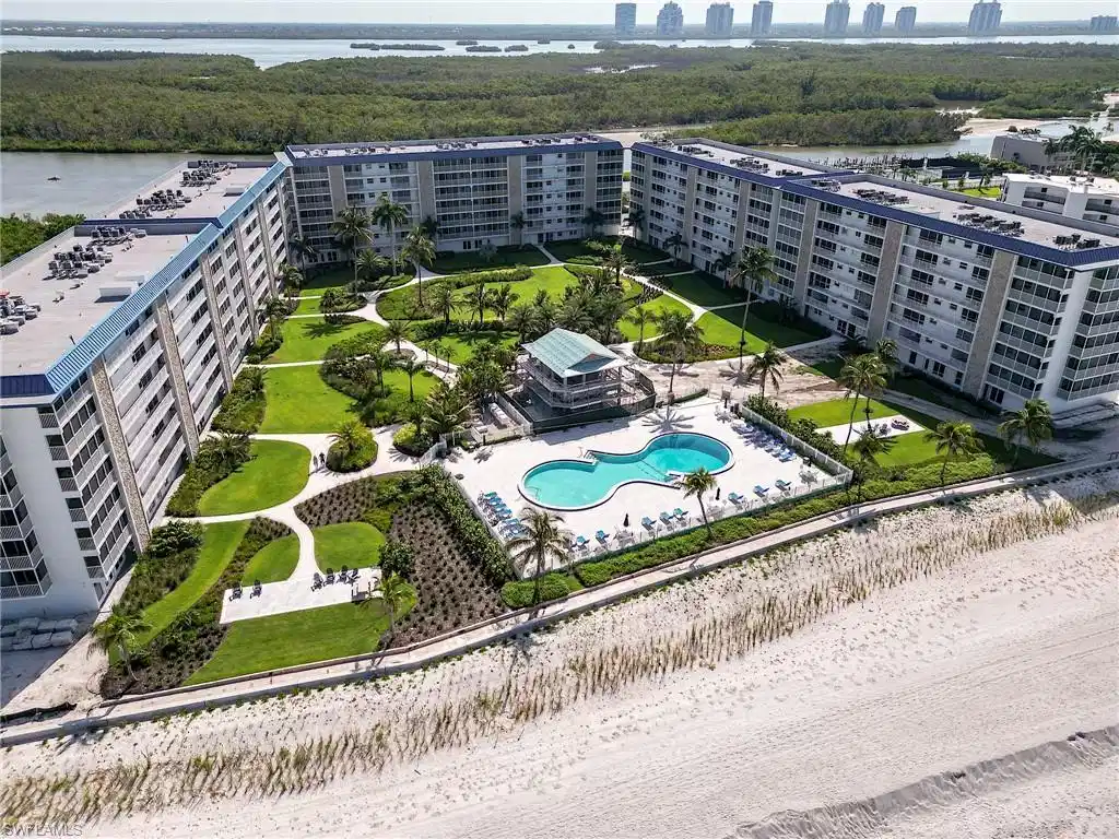 Image 1: Coastal condominium complex with multiple buildings, an expansive manicured lawn, a kidney-shaped swimming pool, a beachfront location, and a surrounding tropical landscape