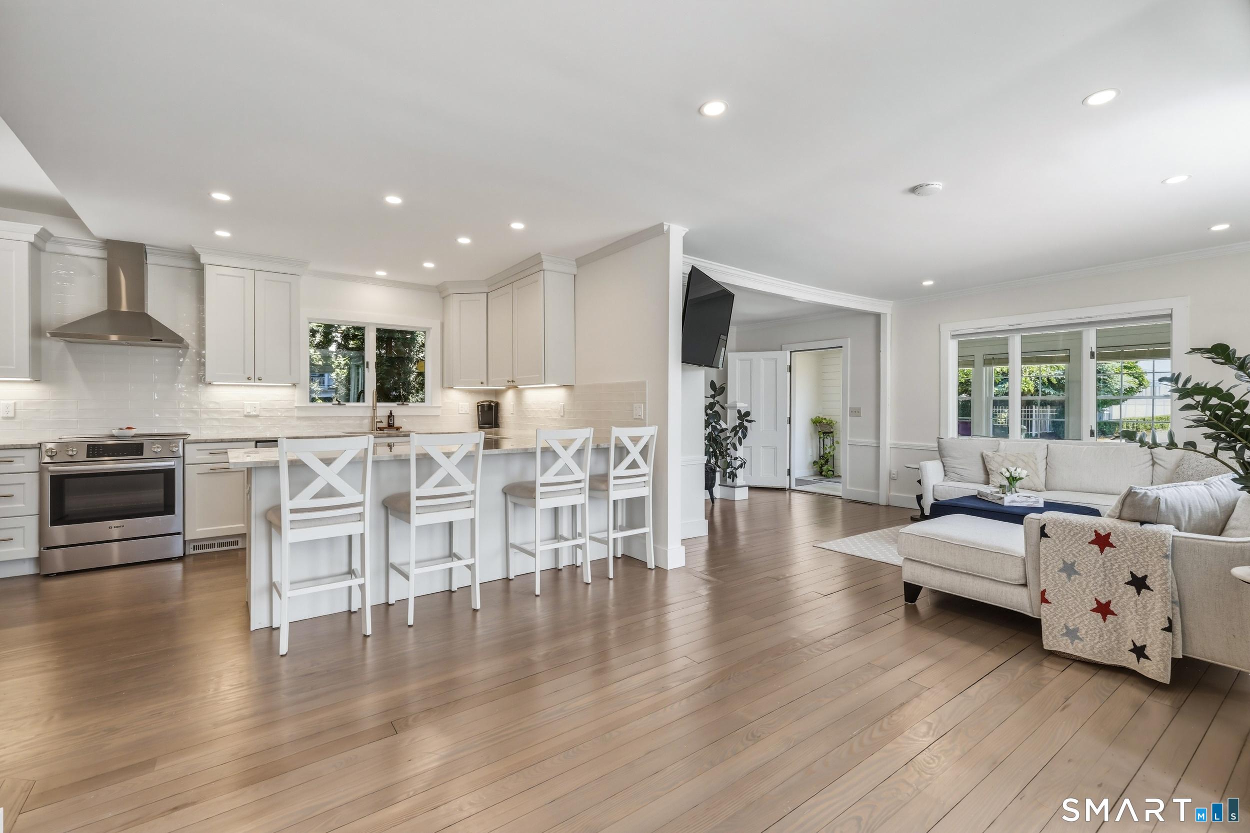Image 4Living Room: Entryway opens to an airy open-concept interior filled with natural light. Beautiful wood flooring, crown molding, and recessed lighting create a warm yet refined atmosphere, while a striking palladium window serves as a stunning focal point.