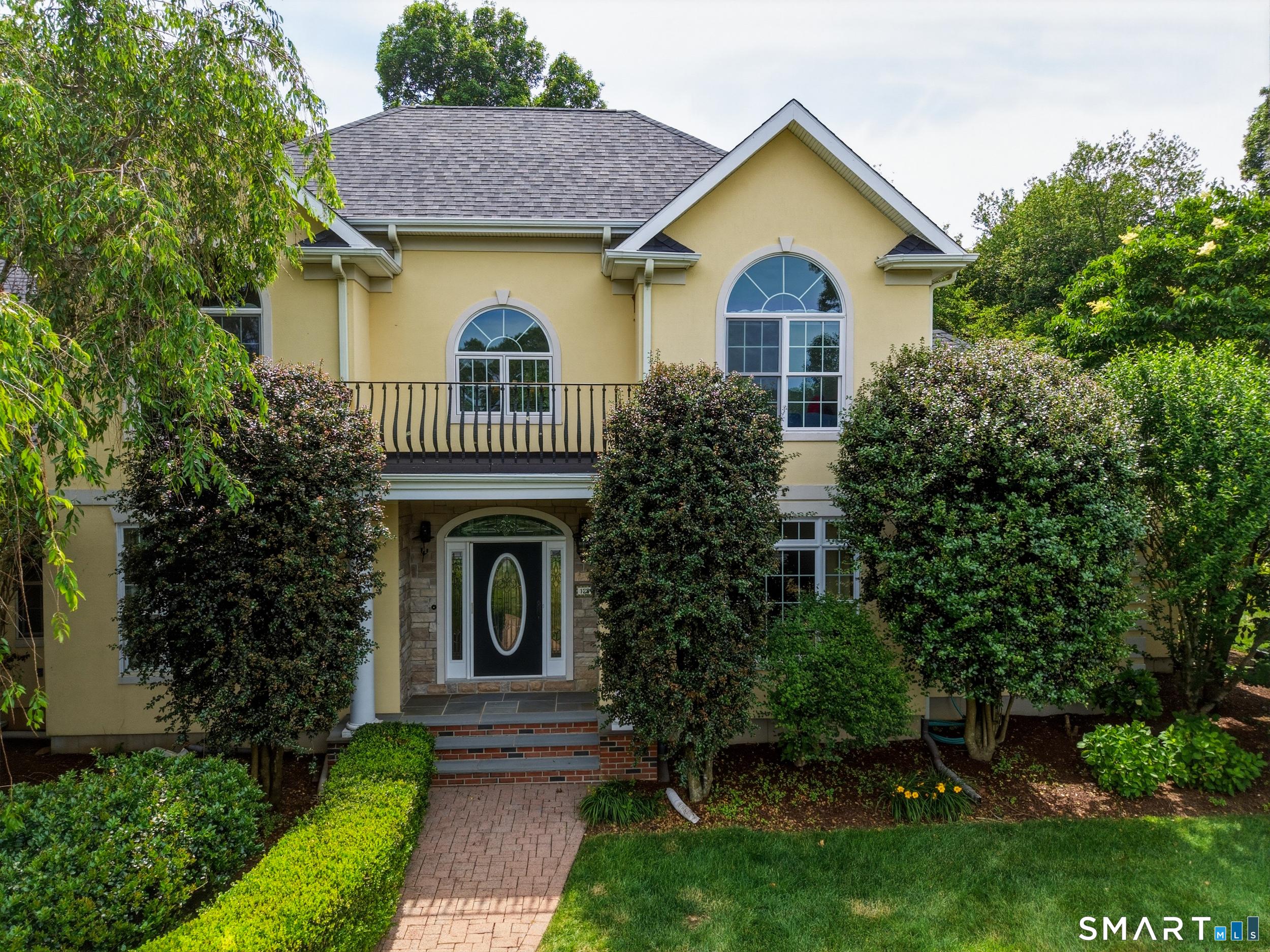 Image 3Front of House: Brick paver walkway leads to the front entrance of this distinctive stucco home, accented by stone detailing on the covered front porch. Above the entry, a charming balcony adds architectural character and timeless curb appeal.